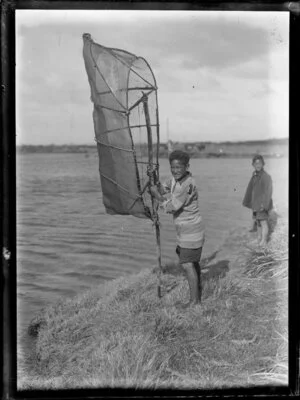 Whitebaiting, featuring two unidentified Maori boys with a whitebait net on banks of unidentified river, Bay of Plenty Region