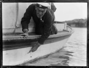 Unidentified swordfisherman, who is smoking a pipe, points to gouges taken out of the side of his boat, Bay of Islands, Far North District, Northland Region