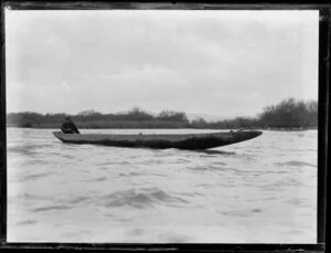 Duck shooting, featuring unidentified hunter in boat on water, with reeds and trees in the background, location unknown