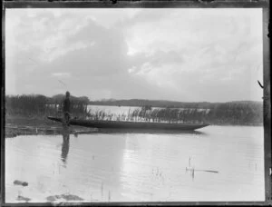 Duck shooting, featuring unidentified hunter, who is holding a gun, at edge of water beside boat, location unknown