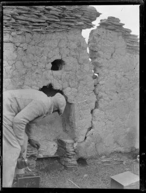 Gold mining, featuring unidentified man inspecting ruins of earth and stone hut, Otago Region