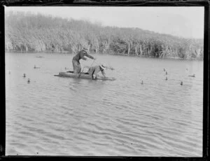 Duck shooting, featuring two men on a raft who are setting decoy ducks in the water, location unknown