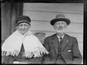 Unidentified elderly couple, in which the woman is wearing a knitted shawl and hat and the man is wearing a three-piece suit, location unknown