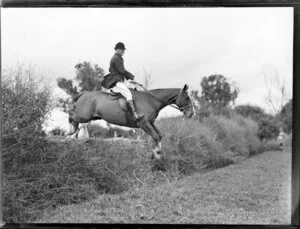 Unidentified man and horse jumping a wall during the Pakuranga point to point hunt, Auckland