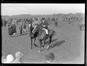 Two unidentified men on horseback amongst the crowds at the Pakuranga point to point hunt, Auckland