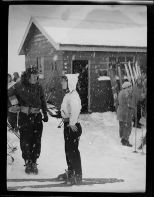 Unidentified man and boy talking outside Happy Valley Chalet during snowfall while skiing on Coronet Peak, Otago