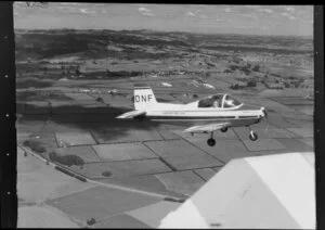 Auckland Aero Club Airtourer aircraft (DNF) flying over farmland in the Auckland area, including pilot, an unidentified man, visible