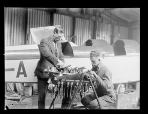 Two unidentified men doing mechanical work on aircraft engine