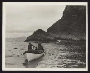 Three men in boat in ocean with rocks in background