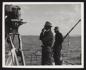 Stacy Woodard and unidentified man standing on metal whale boat with camera tripod and harpoon in view