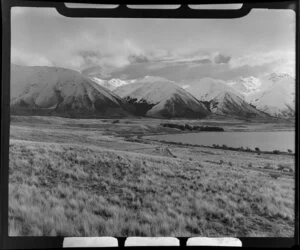 Tussock covered hills beside Lake Ohau, Waitaki County, with snow covered mountains beyond