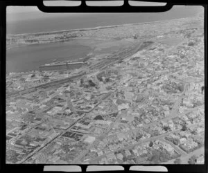 Close-up view showing Dunedin City Centre, with the Octagon with Saint Paul's Anglican Cathedral, residential and commercial buildings, railway station and inner harbour with dock area, wharves and ships, to Saint Clair Beach beyond