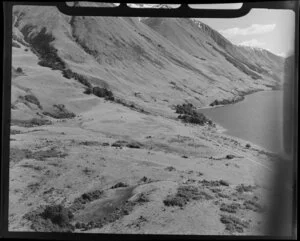 Lake Ohau, Central Otago, view of lake edge with road below steep mountains slopes, foreground evaporated pond on high country sheep run with drovers hut and landrover just beyond