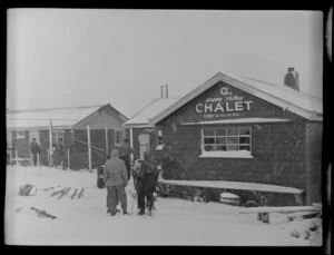 People standing outside the Happy Valley Chalet in a snowfall, Coronet Peak, Otago