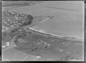 Orakei, Auckland, view of Maori settlement at Orakei Domain, Okahu Bay, with beach and Tamaki Drive with several houses and meeting house on scrubland foreground next to sports field, residential houses surround with Royal Akarana Yacht Club and Hobson Bay beyond