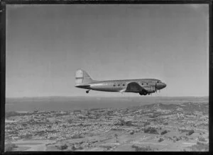 New Zealand National Airways Corporation (NAC) Flagship Dakota aircraft in flight over Auckland, showing City and wharves