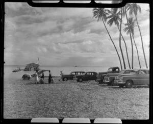 Satupuala Base, Upolu, Samoa, showing men, cars and the TEAL (Tasman Empire Airways Limited) ZK-AMM flying boat in the distance