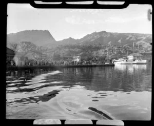 Locals watch from waterfront as TEAL (Tasman Empire Airways Limited) flying boat departs Tahiti, showing boats, buildings and hills