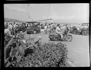 Street scene with police officer on motor bike, people standing watching a passenger boat go past, Papeete, Tahiti