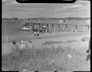 Beach scene at Paihia, Bay of Islands, showing cars being transported by ferry and people on the wharf