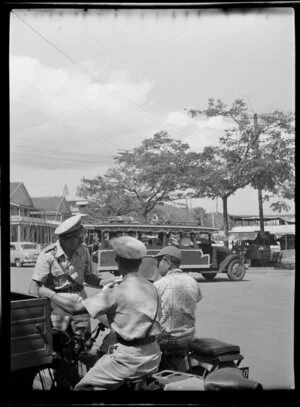 Street scene with two police officers talking to a man on motor scooter and a passenger bus going past, Papeete, Tahiti