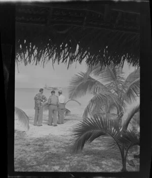 Beach scene, including three unidentified men, flying aircraft boat at sea, Akaiami, Aitutaki, Rarotonga