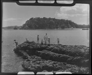 Man and children fishing on a rock at Paihia, Bay of Islands, Northland, probably Motumaire Island in the background