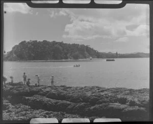 Man and children fishing on a rock in Paihia, Bay of Islands, Northland, probably Motumaire Island in the background