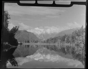 Woman and child in dinghy on Lake Matheson, with reflection of Fox Glacier, West Coast