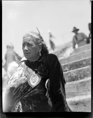 Unidentified Maori elder woman, with Ta Moko from Ngati Awa Taranaki, wearing one feather in hair, traditional Maori cloak, heart shape greenstone pendant with silver ferns and the word Kia Ora, Royal reception celebrations, Rotorua