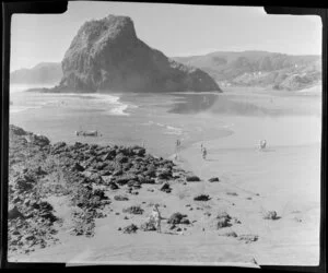 Beach at Piha, Auckland, showing people, dinghy and Lion Rock