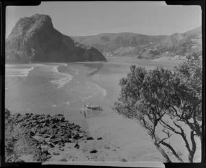Beach at Piha, Auckland, showing Lion Rock and people pushing a dinghy on a trailor