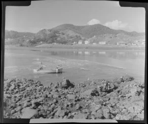 Beach at Piha, Auckland, showing people in a dinghy and houses in the distance
