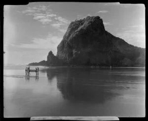 Beach at Piha, Auckland, showing Lion Rock and people carrying a dinghy