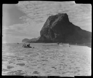 Beach at Piha, Auckland, showing Lion Rock and people in a dinghy and swimming