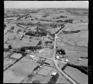 Waimauku, Auckland, showing intersection of State Highway 16 with Muriwai Road and Waimauku-Station Road, with school, tennis courts and lawn bowls, farmland beyond