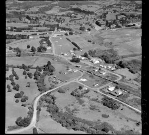 Waimauku, Auckland, showing intersection of State Highway 16 with Muriwai Road and Waimauku-Station Roads, with school, train with carriages, farmland beyond