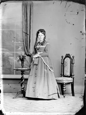 Unidentified woman with her hair in ringlets, holding a small book and wearing a corduroy dress with trimmings and ornate buttons