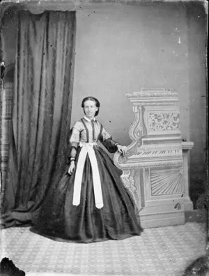 Unidentified woman in an ornate dress with a light-coloured bodice and a full, dark skirt, with a white sash