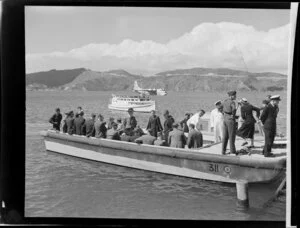 Unidentified passengers and Tasman Empire Airways Limited crew disembark at the flying boat base near Hataitai Beach, Wellington, with the Short S.45 Solent flying boat, R.M.A Araragi (ZK-AMM), moored in Evans Bay in the background