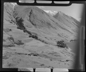 Lake Ohau, Central Otago, view of lake edge with road and steep mountain slopes with snow feed creek, foreground high country sheep run with drovers hut and landrover