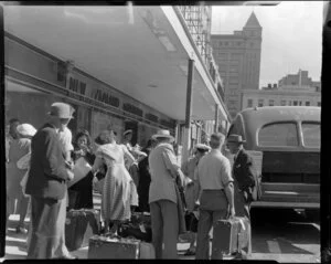 Passengers outside New Zealand National Airways Corporation building waiting to board bus