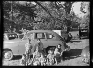 Unidentified group of adults and children beside a car at at Ferndale, Henderson, Auckland