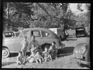 Unidentified group of adults and children beside a car for a picnic at Ferndale (Carey Park), Henderson, Auckland