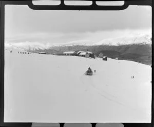 Man on a caterpillar tractor with a dog leaving the chalet, Coronet Peak, Otago