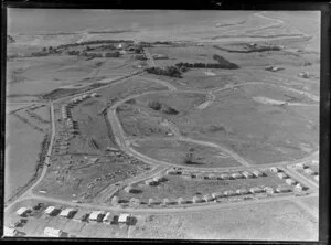View of new housing development Glen Innes, Auckland City, showing new houses under construction and vacant sites and road layout, with farmland and country estate residential building surrounded by trees and tidal estuary beyond