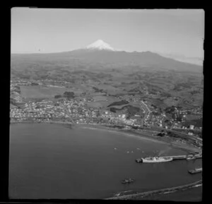 View over New Plymouth Harbour, Port Taranaki, with ship at wharf and residential housing and oil storage tanks back from beach, farmland to Mount Taranaki and Pouakai Range beyond