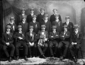 Group portrait of men in suits and straw boaters, with teddy bear mascot