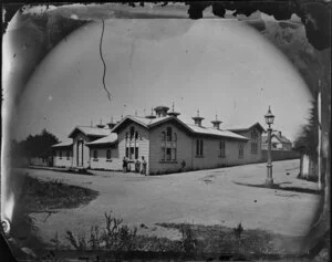 Exterior view of a large wooden building on Museum Street, Thorndon, Wellington, with unidentified persons standing on street