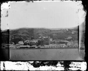 View of Wellington, from a pier near the site of the Wellington Railway Station, showing buildings along Lambton Quay including Sweeney's Nelson Hotel, a manufacturing confectioner, and houses on hill behind